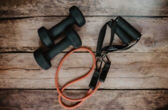A selection of compact fitness gear arranged in a small home workout space, including resistance bands, dumbbells, and a yoga mat.